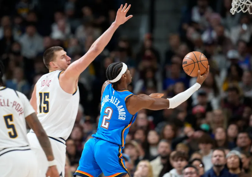 Oklahoma City Thunder guard Shai Gilgeous-Alexander, right, gets past Denver Nuggets center Nikola Jokic (15) to the basket in the first half of an NBA basketball game Friday, Dec. 29, 2023, in Denver. (AP Photo/David Zalubowski)